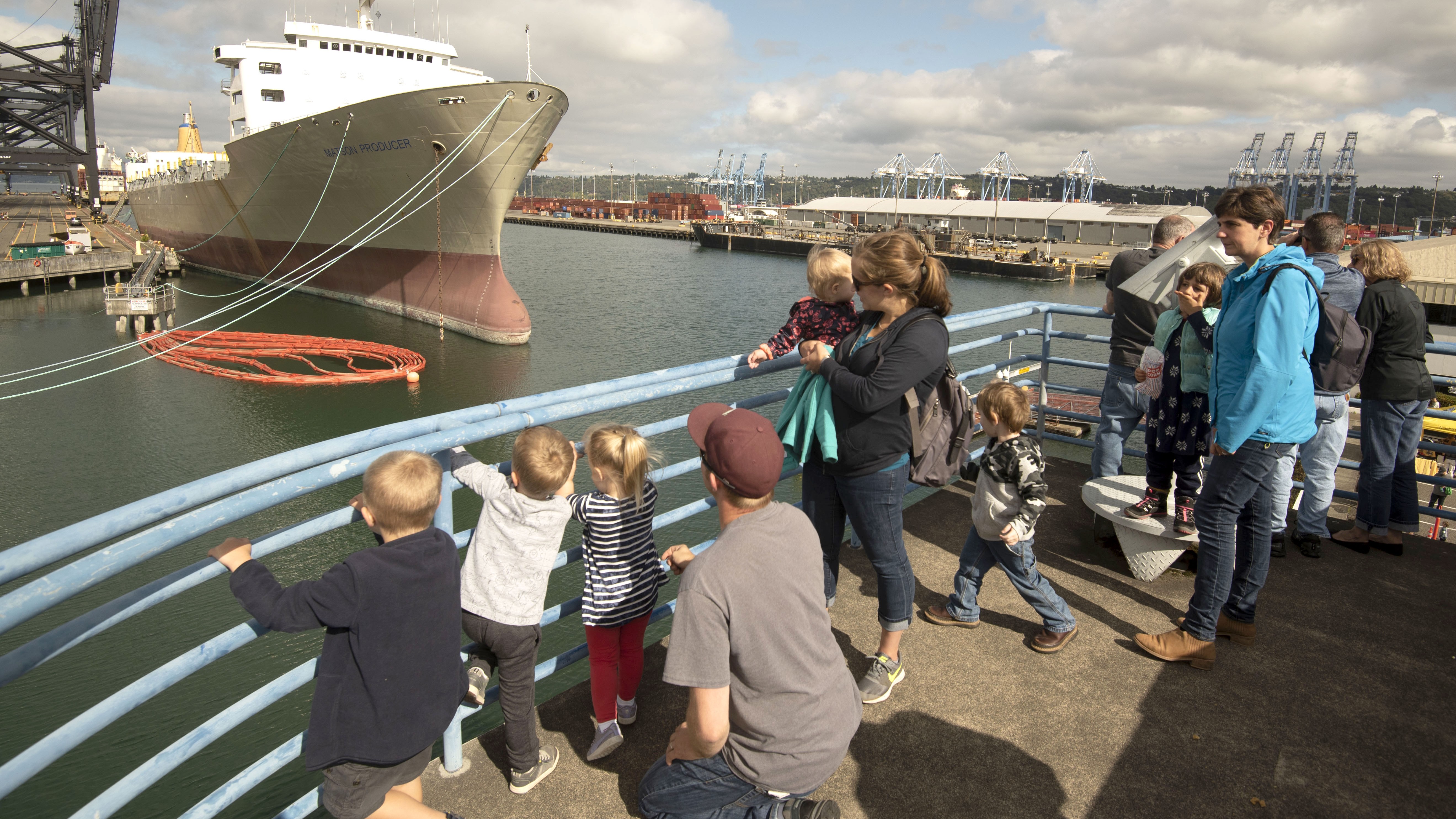 A group of people look over a boat railing at another boat in the sun.
