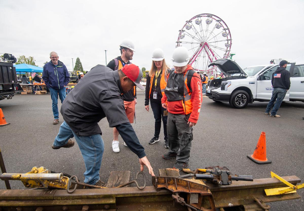 Students in protective gear looking at a technician explaining the parts of a rail track.