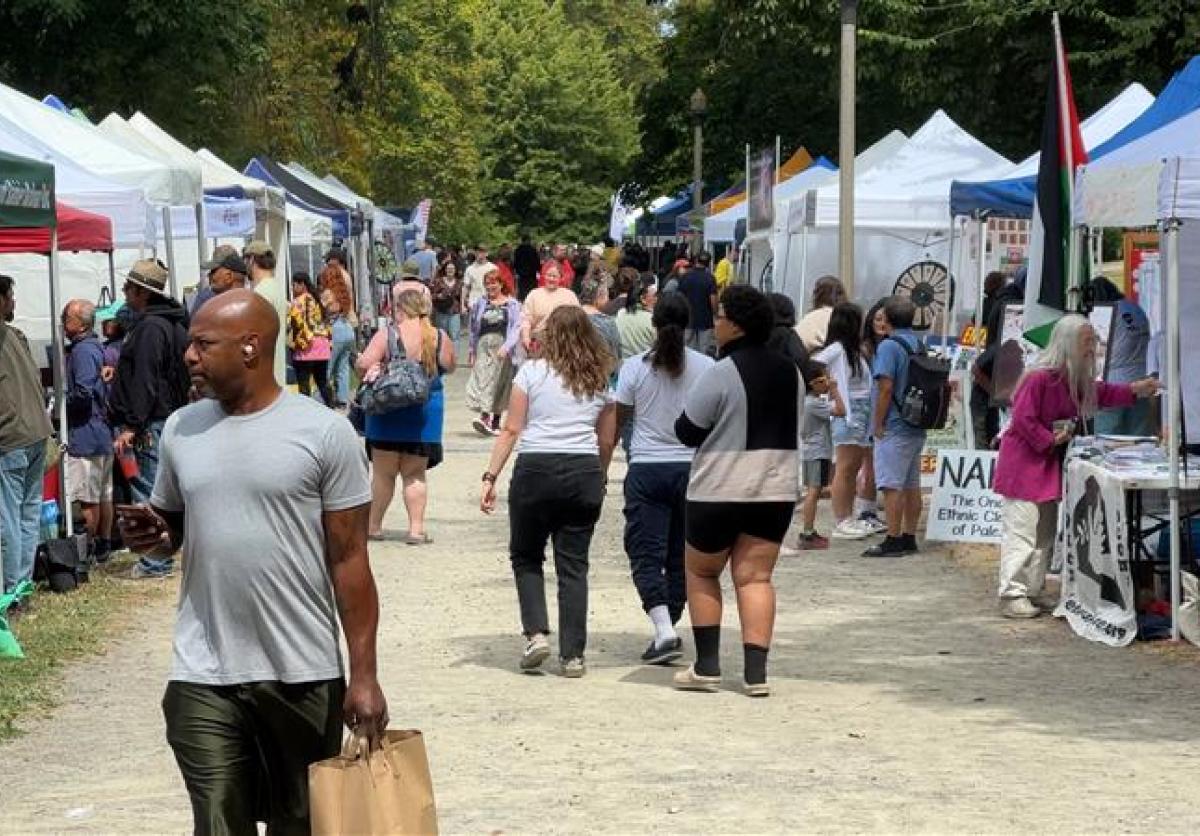 A man in a grey shirt walks through a group of booths at an outdoor event.
